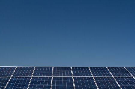 A long row of solar panels generating clean, renewable energy under a clear, blue sky.の写真素材