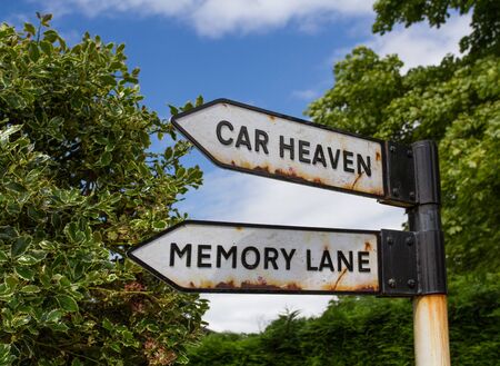 A rusty road sign in the countryside pointing the way to Car Heaven and Memory Lane.