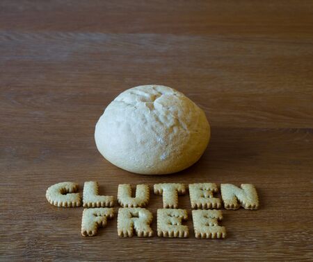 An artisan loaf of gluten free bread on a wooden table with the phrase Gluten Free spelled out with alphabet shaped cookies below.の写真素材