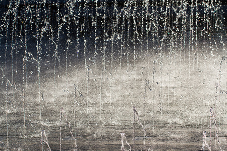 Jets of cold, clear water spurting upwards into the air and splashing onto the ground in a water fountain, high contrast background.の写真素材