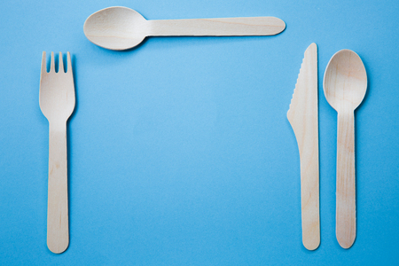 A variety of recyclable wooden cutlery set for a place setting including knife, fork and spoon on a blue background with copy spaceの写真素材