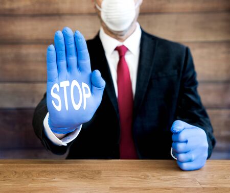 A concept of a businessman or doctor wearing ppe including blue gloves and facemask to stop and self isolate or social distance during the Coronavirus pandemic.の写真素材