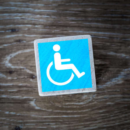 A blue disabled sign, symbol or icon for mentally disabled and physically disabled people on a wooden block with a wood background and copy spaceの写真素材