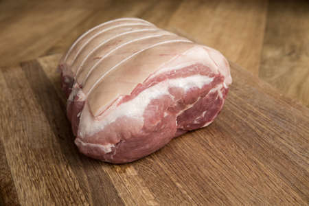A close up of a raw cut of meat called a Pork Shoulder tied up and rolled with butcher's string with its skin scored ready for crackling on a wooden butcher block with copy spaceの写真素材