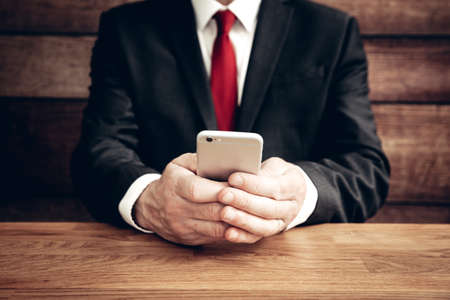 A midsection of a male wearing a suit and holding a mobile phone in his hands whilst texting or using social media with copy spaceの写真素材