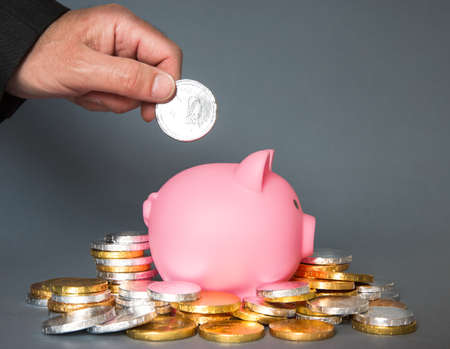 A male hand putting money in a piggy bank to save for the future with copy spaceの写真素材