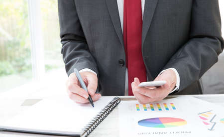 A midsection of a businessman at his desk analysing and calculating business costs and accounting with company profits with copy spaceの写真素材
