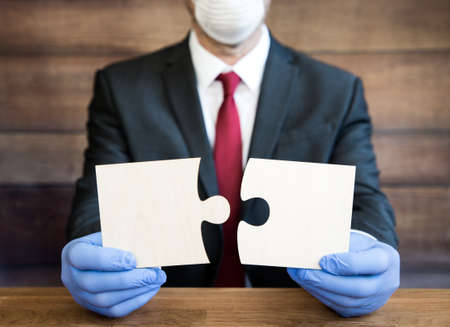 A male businessman wearing pipe, face mask and gloves during the Coronavirus outbreak and holding a jigsaw puzzle with copy spaceの写真素材