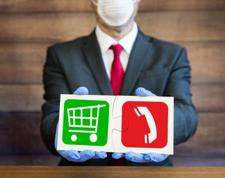 A businessman holding a jigsaw puzzle sign with a retail shopping trolley and a mobile phone denoting the difficulties faced by online stores during the Coronavirus lockdown pandemicの写真素材
