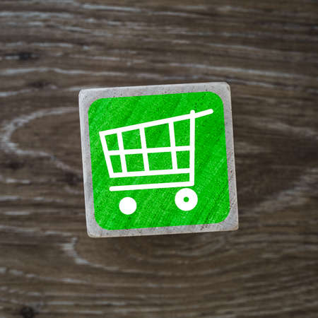 A green shopping cart sign, symbol or icon representing store retail and consumerism on a wooden block with copy spaceの写真素材