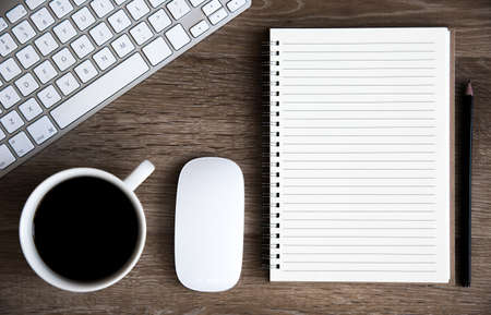 A high angle view of a home office desk with keyboard, coffee, mouse and spiral notebook with lined copy space for notesの写真素材