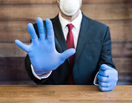 A Doctor or businessman wearing ppe blue gloves and face mask during the Coronavirus Pandemic gesturing people to stay away and social distance when ppe is in short supplyの写真素材
