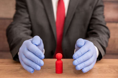 A Coronavirus concept of a man wearing blue, surgical gloves shielding and protecting a worker,...