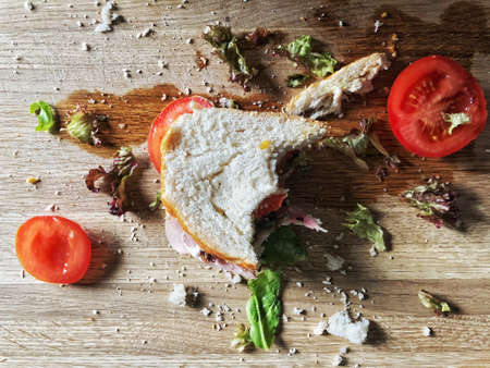 Food waste background of half eaten salad sandwich leftovers on a wooden table