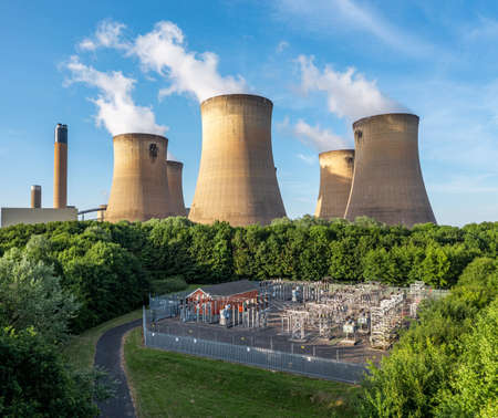 aerial view of the cooling towers and chimney of a coal fired power station generating electricity with electrical equipment to supply power to the national Grid via transformersの写真素材
