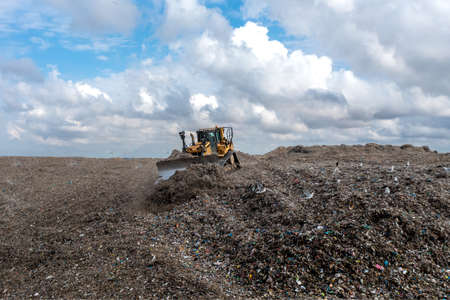 A Bulldozer machine moving waste and household garbage on a large landfill heapの写真素材