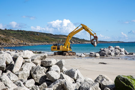 Mechanical diggers on a construction site repairing coast defences and sea walls with rocks from a quarry after rising sea levels caused erosion and damageの写真素材