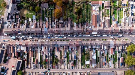 Aerial view directly above a long city street lined with run down terraced houses and gardens with...