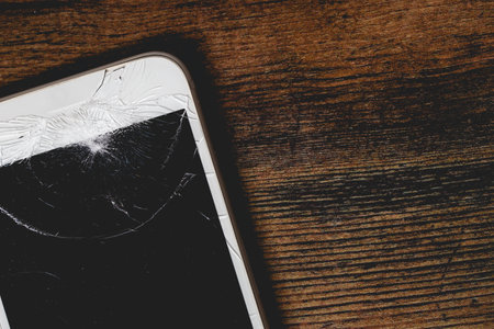 A close up of a damaged mobile phone with cracked screen for repair on a wooden background with copy spaceの写真素材