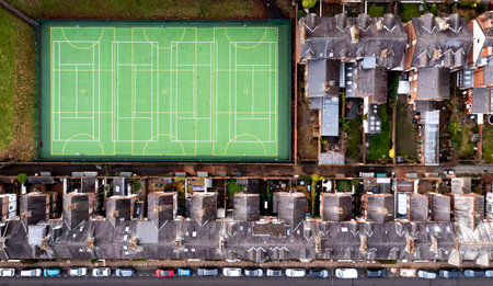 An aerial view directly above of the rooftops of back to back terraced houses in a UK suburb with a local community sports pitch for amateur useの写真素材