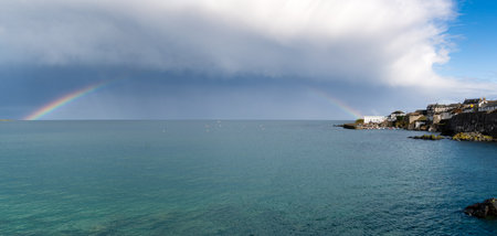 Landscape view of a rainbow and story skies over the picturesque Cornish fishing village and harbour of Coverackの写真素材