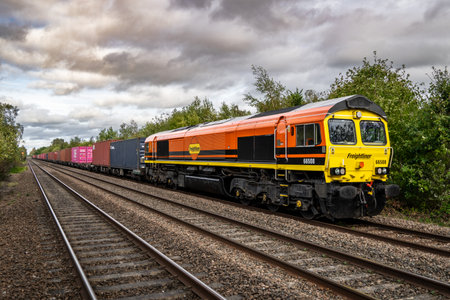DERBY, UK - OCTOBER 6, 2023.  A Freightliner Intermodal Class 66 freight train with container box on a main line railway painted in the parent company of Genesee and Wyoming liveryのeditorial素材
