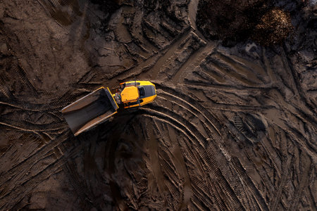 Aerial view directly above an industrial dumper truck or earth mover vehicle with muddy soil and...