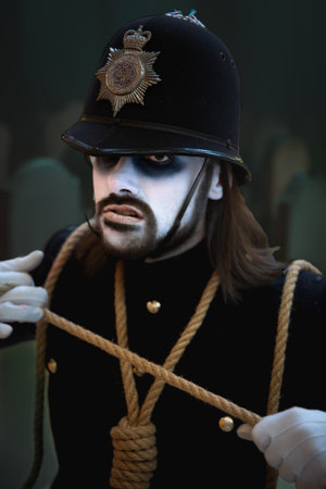 A close up portrait of a male cosplayer at a comic con event in a scary British Police uniform with white painted face in a Halloween conceptの写真素材