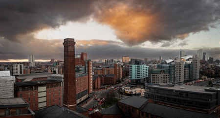 An aerial panoramic view of a Leeds cityscape skyline in West Yorkshire with historic warehouse chimney and modern apartment buildings under a dramatic sky at sunriseの写真素材
