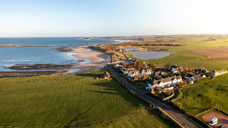Aerial panorama landscape view of The England Coast Path along Embleton Bay beach at Newton-By-The-Sea village at sunsetの写真素材