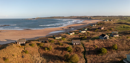 Aerial panorama landscape view of remote beach hut with a sea view on the Northumbrian sand dunes over looking Embleton Bay and Dunstanburgh Castle at sunsetの写真素材