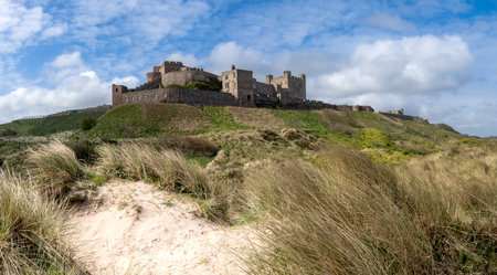 BAMBURGH CASTLE, NORTHUMBERLAND, UK - APRIL 23, 2024. Landscape panorama view of Bamburgh Castle and sand dunes on the beautiful Northumberland coast with blue sky and sunshineのeditorial素材