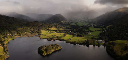 Aerial panoramic landscape of the village and lake of Grasmere in The Lake District National Park with calm water and sunshine in the valley and a brooding storm on the hillsの写真素材