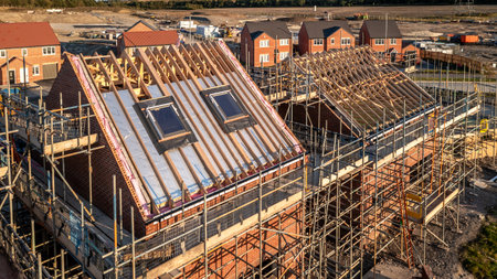 Aerial view of a roof under construction with beams and apex supporting exterior skylight windows on a new build house surrounded by scaffolding on a construction siteの写真素材