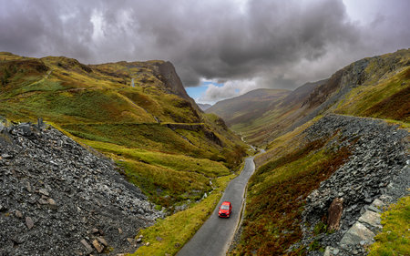 A landscape view of a car reaching the top of the B5289 Honister Pass road from The Honister Slate Mine in The Lake District National Park on a sunny Summer dayの写真素材