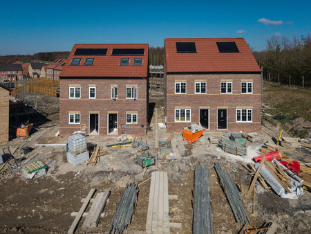 A row of characterless new build houses on a construction site with in built rooftop solar panels for affordable and sustainable energy to keep utility bills downの写真素材