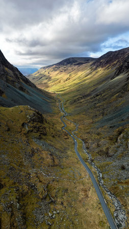 Aerial vertical panorama landscape view of the Honister Pass road in The English Lake District National Park in Cumbria, UK with surrounding mountains winding it's way to the Honister Slate Mineの写真素材