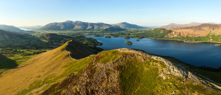 Aerial panorama landscape of the walking path along the top of Catbells mountain ridge in the English Lake District National Park with Derwent Water lake and Keswick town below the Northern Fells on a sunny dayの写真素材