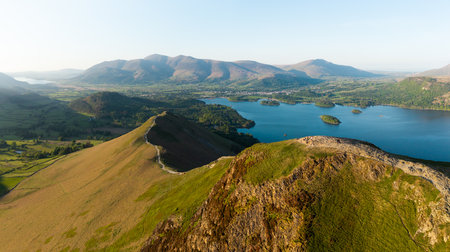 Aerial panorama landscape of the walking path along the top of Catbells mountain ridge in the English Lake District National Park with Derwent Water lake and Keswick town below the Northern Fells on a sunny dayの写真素材