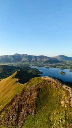Aerial vertical landscape of the walking path along the top of Catbells mountain ridge in the English Lake District National Park with Derwent Water lake and Keswick town below the Northern Fells on a sunny dayの写真素材