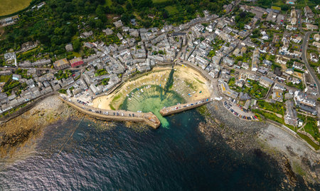 Aerial landscape view directly above of the quaint Cornish fishing village of Mousehole on the Lizard Peninsula in Cornwall with rocky coastline and historic harbourの写真素材
