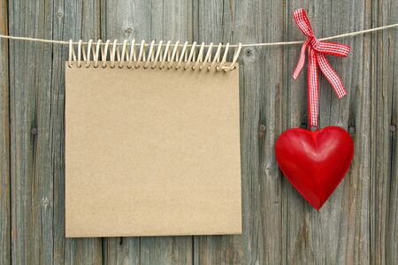 notepad with a heart made &#8203;&#8203;of sheet metal hanging in front of wooden wallの写真素材