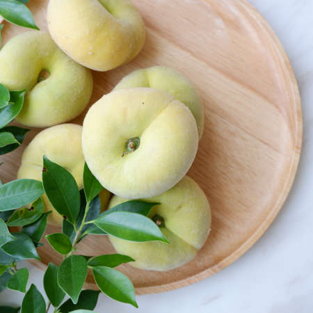 Flat peaches in wooden plate.の写真素材