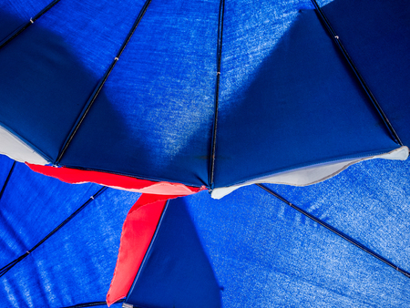 Under big blue umbella on the beach safety from UV. Show feeling sit under umbella.の写真素材