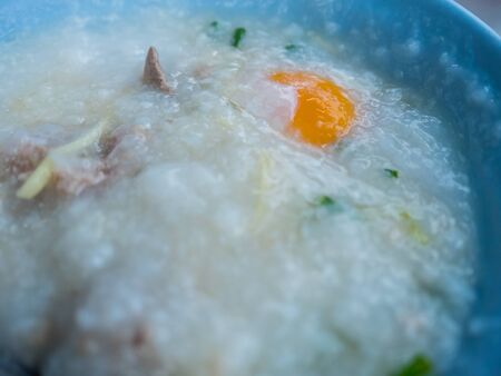 Rice soup with pork and egg in blue bowl.