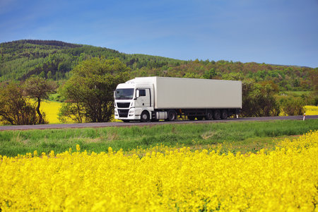White truck on the road with yellow rape flowers in the background.の写真素材