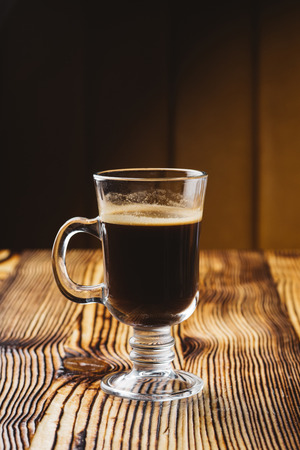 glass coffee cup on rustic textured wooden table with dark lightの写真素材