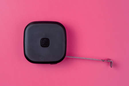 Measuring tape for construction work. Black roulette on a pink isolated backgroundの写真素材