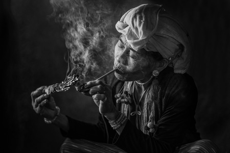 CHIANG MAI, THAILAND - JUL 25 : Karen hill tribe is smoking tobacco pipe with traditional clothes and dramatic light on July 25, 2015 in Chiang Mai, Thailand.のeditorial素材