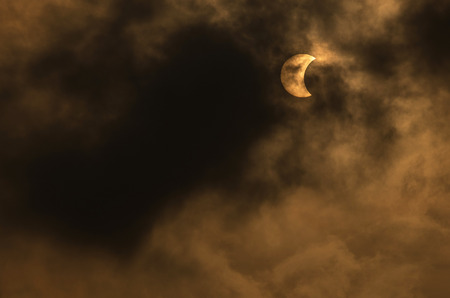 The Moon covering the Sun in a partial eclipse with dramatic cloud. Scientific background,...
